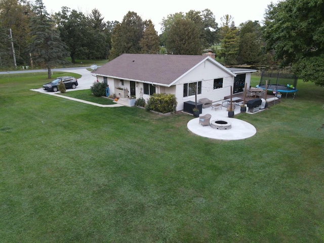 rear view of property featuring a yard, a chimney, an outdoor fire pit, and a trampoline