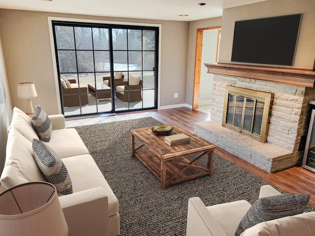 living area featuring a stone fireplace, wood finished floors, and baseboards