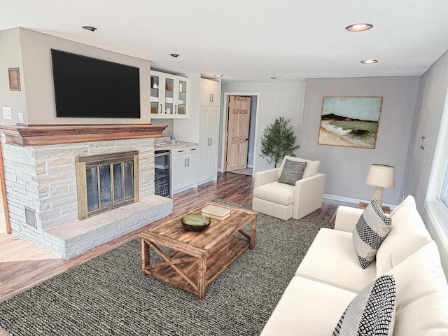 living area with wood finished floors, baseboards, recessed lighting, a stone fireplace, and wine cooler