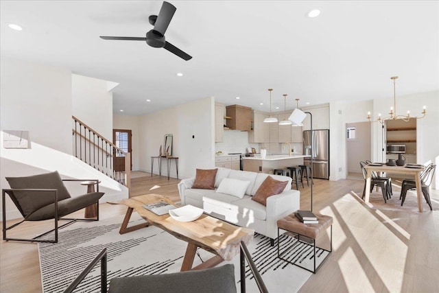 living area featuring light wood-style flooring, ceiling fan with notable chandelier, recessed lighting, stairway, and baseboards