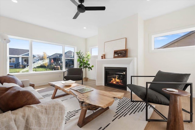 living room with a ceiling fan, wood finished floors, baseboards, recessed lighting, and a glass covered fireplace