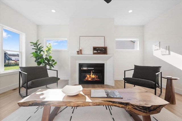 living room featuring recessed lighting, light wood-type flooring, baseboards, and a glass covered fireplace