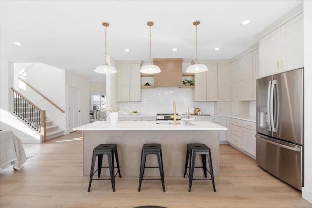 kitchen featuring backsplash, a center island with sink, stainless steel fridge with ice dispenser, and light countertops