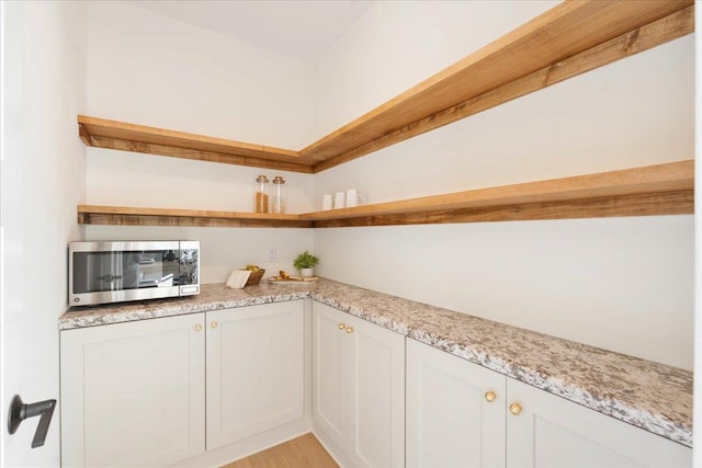 kitchen with white cabinetry, open shelves, stainless steel microwave, and light stone counters