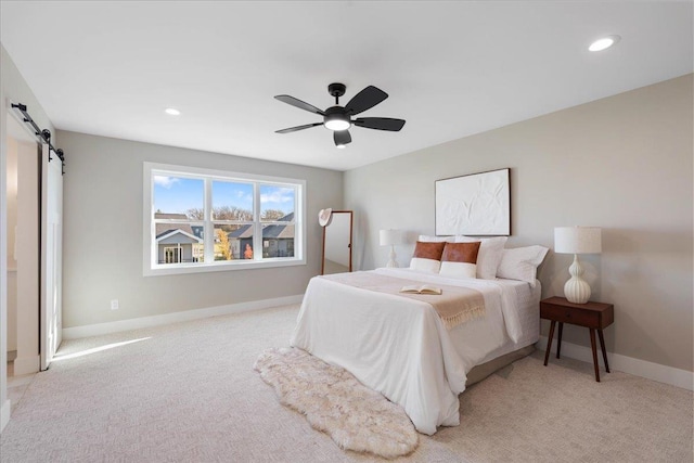 bedroom featuring light carpet, a ceiling fan, recessed lighting, a barn door, and baseboards