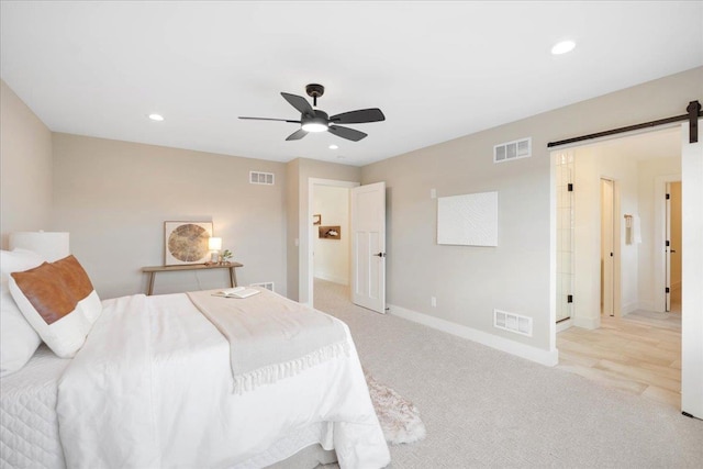 bedroom with visible vents, light carpet, and a barn door