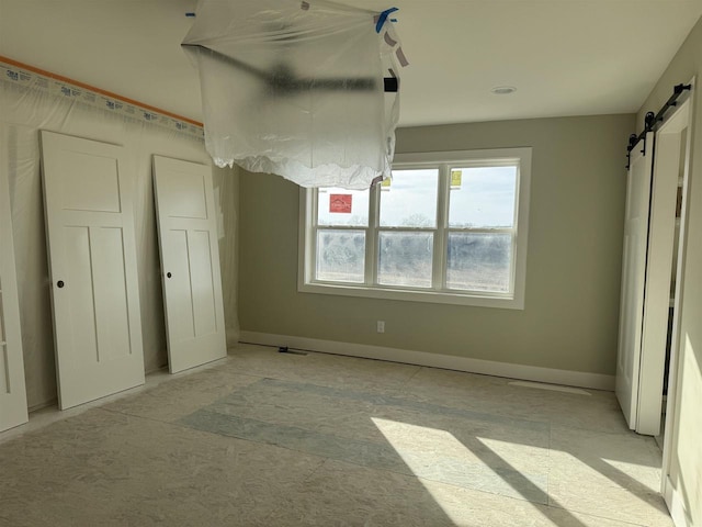 unfurnished bedroom featuring a barn door and baseboards