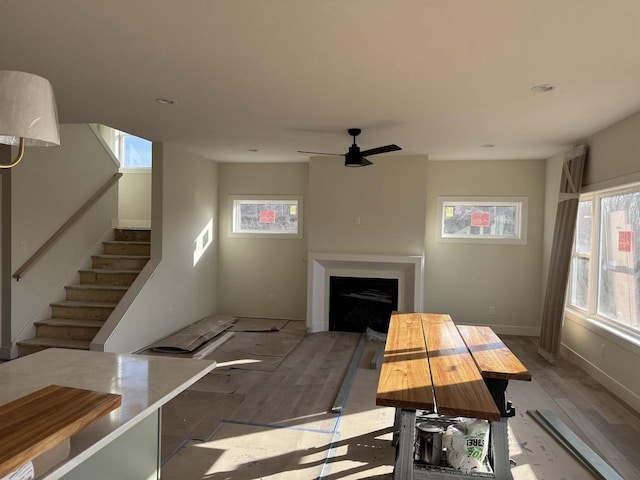 living room with baseboards, stairs, a fireplace, wood finished floors, and a ceiling fan