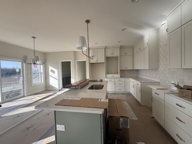 kitchen with a chandelier, backsplash, an island with sink, and a sink