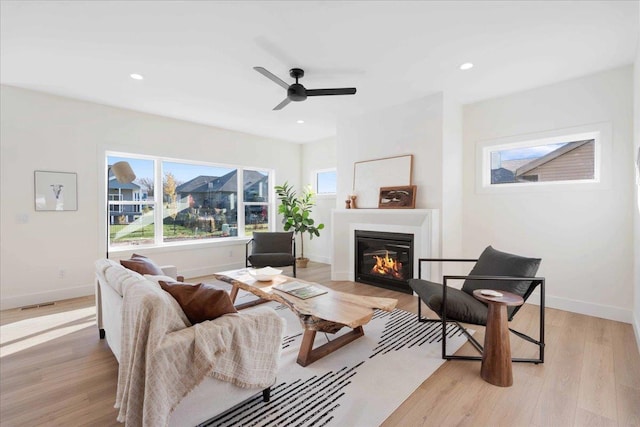 living area featuring a glass covered fireplace, recessed lighting, light wood-type flooring, and baseboards