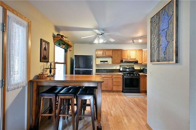 kitchen featuring light wood finished floors, ceiling fan, black appliances, under cabinet range hood, and dark countertops