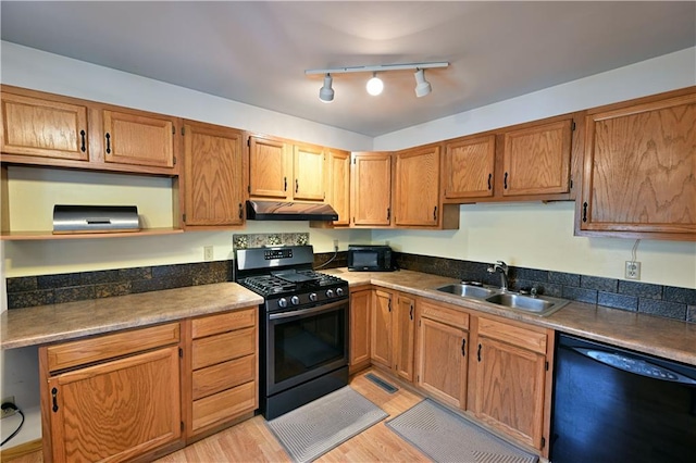 kitchen with under cabinet range hood, light wood-style floors, brown cabinetry, black appliances, and a sink