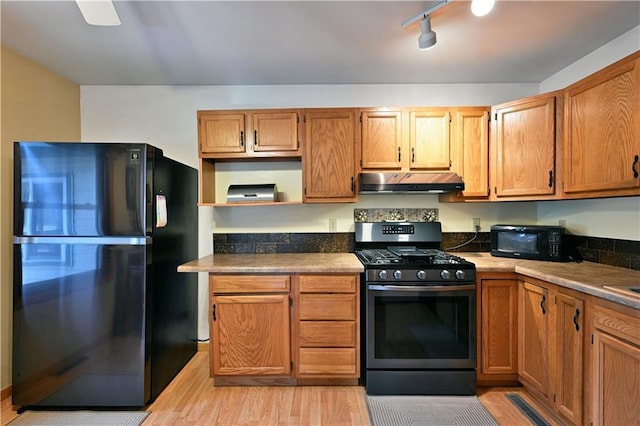 kitchen with light wood-type flooring, black appliances, under cabinet range hood, open shelves, and dark countertops