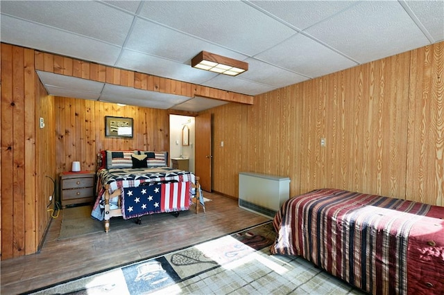 bedroom featuring a drop ceiling, wooden walls, and wood finished floors