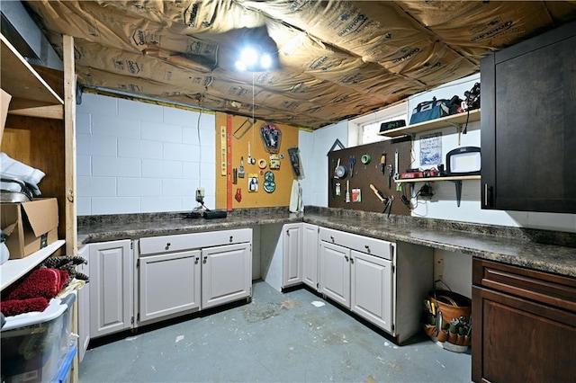 kitchen with open shelves, dark countertops, and concrete floors