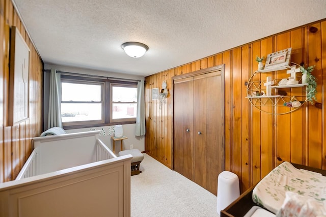 carpeted bedroom with wooden walls, a closet, and a textured ceiling