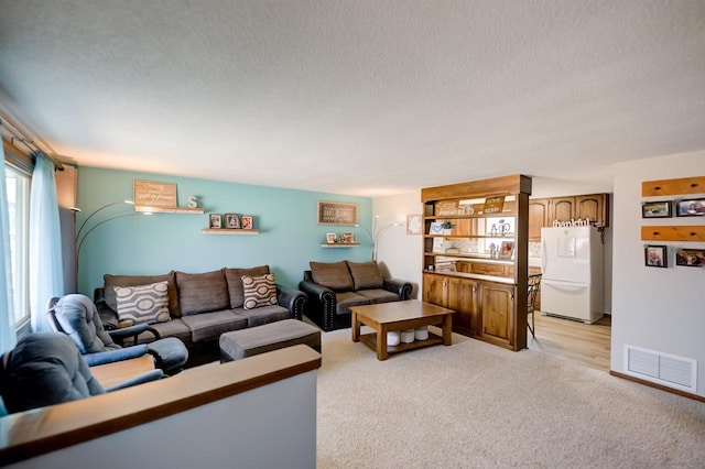 living area with a textured ceiling, visible vents, and light carpet