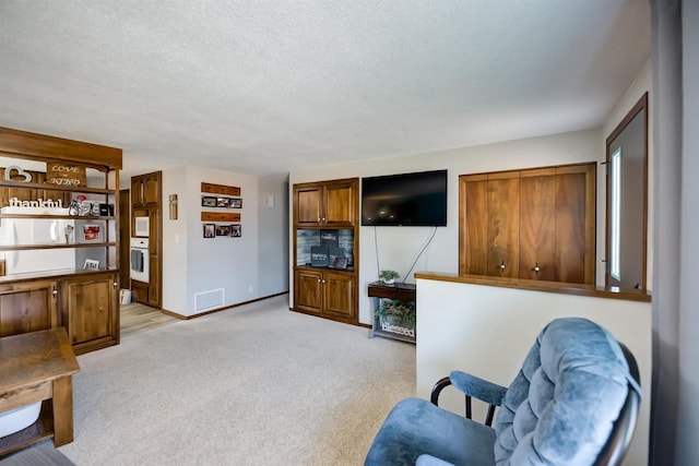 living area featuring baseboards, light colored carpet, visible vents, and a textured ceiling