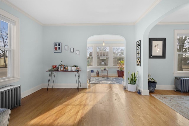 interior space featuring radiator heating unit, wood finished floors, arched walkways, and ornamental molding