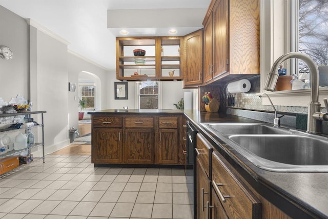 kitchen featuring arched walkways, a peninsula, dark countertops, and a sink