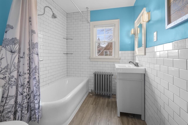 full bath featuring vanity, radiator, shower / bathtub combination with curtain, wood finished floors, and tile walls