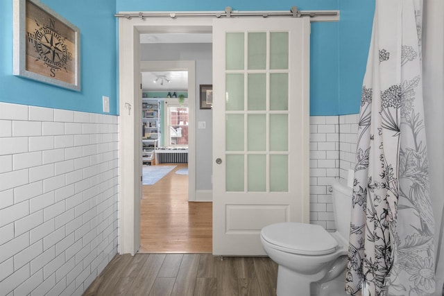 full bath with curtained shower, a wainscoted wall, toilet, wood finished floors, and tile walls