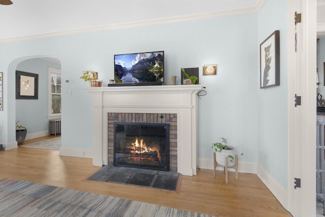 living area featuring radiator, a brick fireplace, baseboards, ornamental molding, and wood finished floors