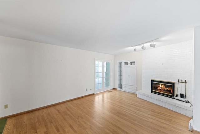 unfurnished living room with rail lighting, a fireplace, baseboards, and light wood finished floors