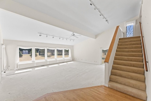 unfurnished living room with beamed ceiling, track lighting, a ceiling fan, wood finished floors, and stairway