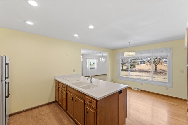 kitchen with a sink, freestanding refrigerator, a peninsula, brown cabinetry, and light wood finished floors