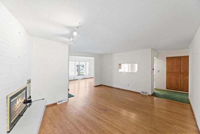 unfurnished living room with visible vents, baseboards, light wood-style floors, and a fireplace