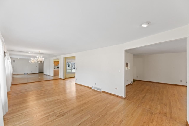 unfurnished living room featuring light wood-style flooring, baseboards, visible vents, and a chandelier