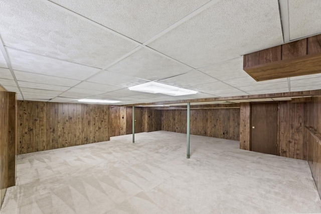 finished basement with a paneled ceiling, wood walls, and carpet flooring