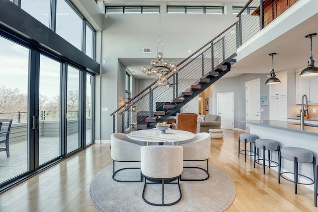 dining area featuring a notable chandelier, light wood-style flooring, baseboards, a towering ceiling, and stairs