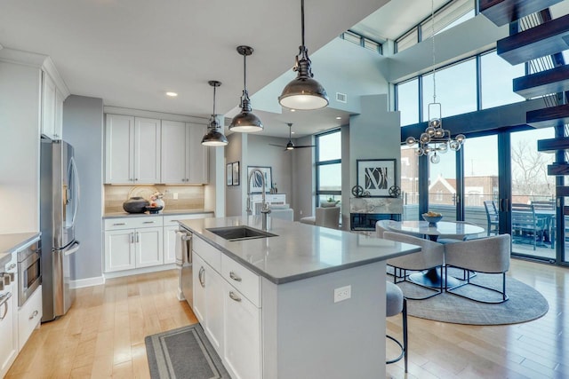 kitchen with light wood-type flooring, decorative backsplash, appliances with stainless steel finishes, a notable chandelier, and a sink