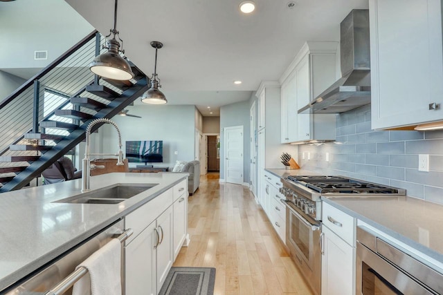 kitchen featuring backsplash, appliances with stainless steel finishes, white cabinetry, wall chimney exhaust hood, and a sink