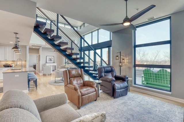 living room with a ceiling fan, visible vents, stairs, light wood-style floors, and expansive windows