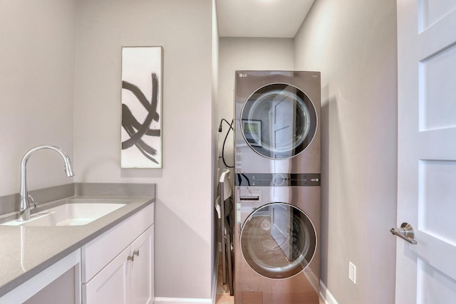 laundry room featuring a sink, stacked washer / drying machine, cabinet space, and baseboards