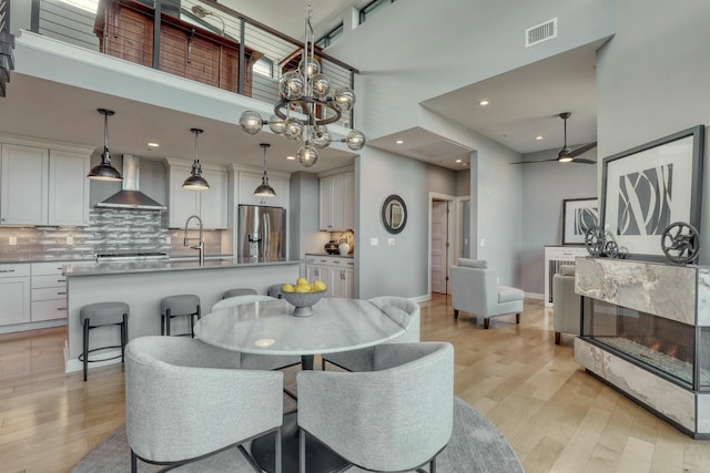 dining room with visible vents, a high ceiling, ceiling fan, and light wood finished floors