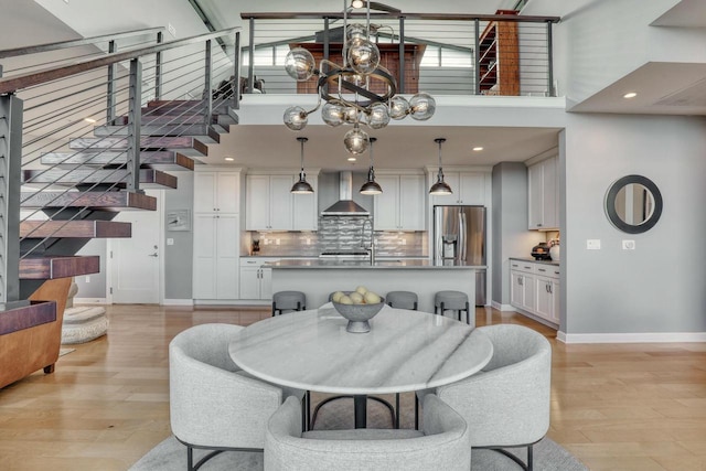 dining room featuring light wood finished floors, high vaulted ceiling, stairs, and baseboards