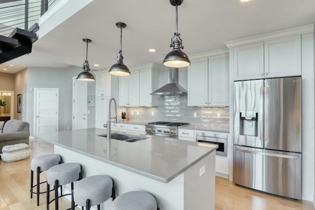 kitchen with a breakfast bar, a sink, decorative backsplash, stainless steel appliances, and wall chimney range hood