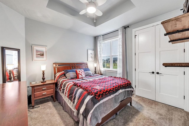 bedroom featuring a raised ceiling, light colored carpet, and ceiling fan