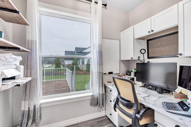 home office featuring baseboards, wood finished floors, and built in study area