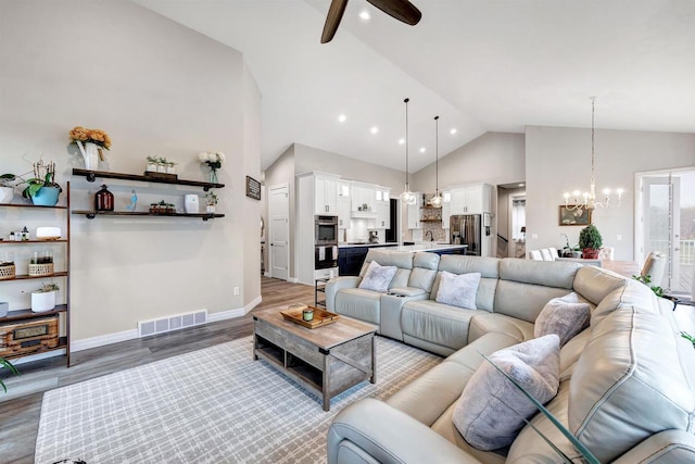 living area with visible vents, baseboards, ceiling fan with notable chandelier, wood finished floors, and high vaulted ceiling