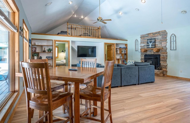 dining area with baseboards, light wood-style flooring, a fireplace, high vaulted ceiling, and a ceiling fan