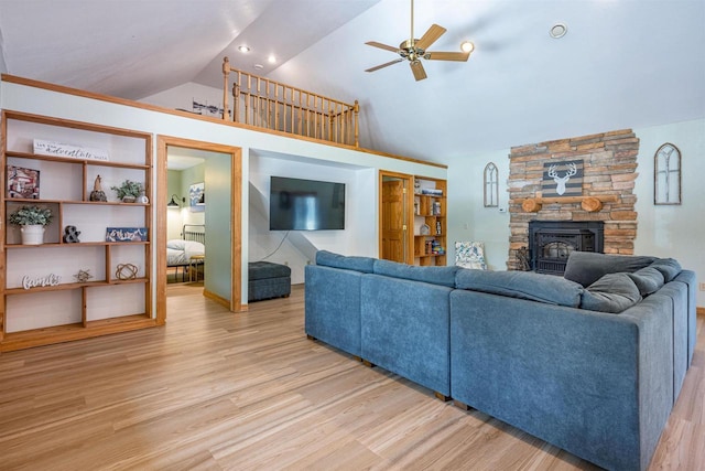 living room featuring a stone fireplace, vaulted ceiling, a ceiling fan, and light wood finished floors