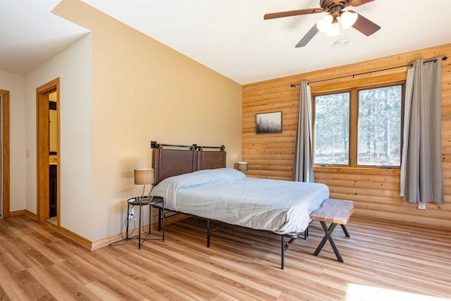 bedroom featuring rustic walls, baseboards, wood finished floors, and a ceiling fan