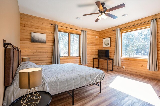 bedroom with log walls, ceiling fan, and wood finished floors