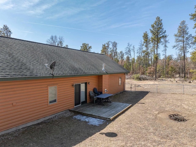 rear view of house with log veneer siding, roof with shingles, a deck, and fence