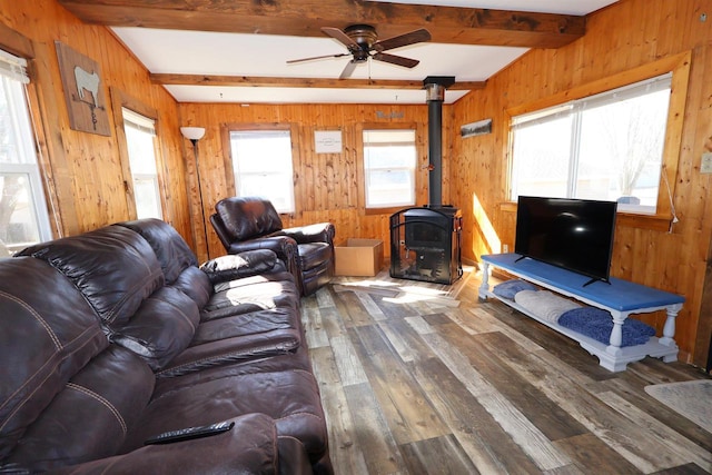 living area with hardwood / wood-style floors, a ceiling fan, beam ceiling, a wood stove, and wood walls